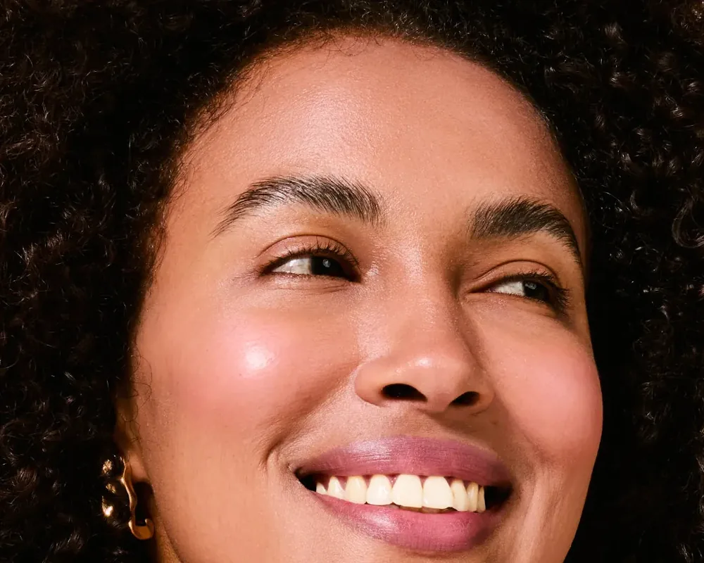 Close do rosto de uma mulher sorrindo com pele uniforme e luminosa